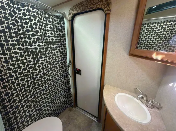 RV rental bathroom with geometric black/white shower curtain, toilet, sink, and frosted door, offering compact convenience.. Crossroads RV Sunset Trail Super Lite 2017