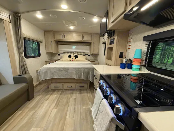 Bright and modern RV rental interior featuring a bedroom with Mickey pillow, compact kitchen, and living space. Ready for adventure!. Forest River Flagstaff Micro Lite 2022