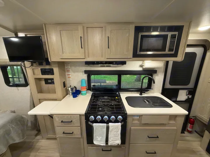 Modern RV rental interior features a functional kitchenette with stove, sink, microwave, ample storage, and TV for convenience.. Forest River Flagstaff Micro Lite 2022