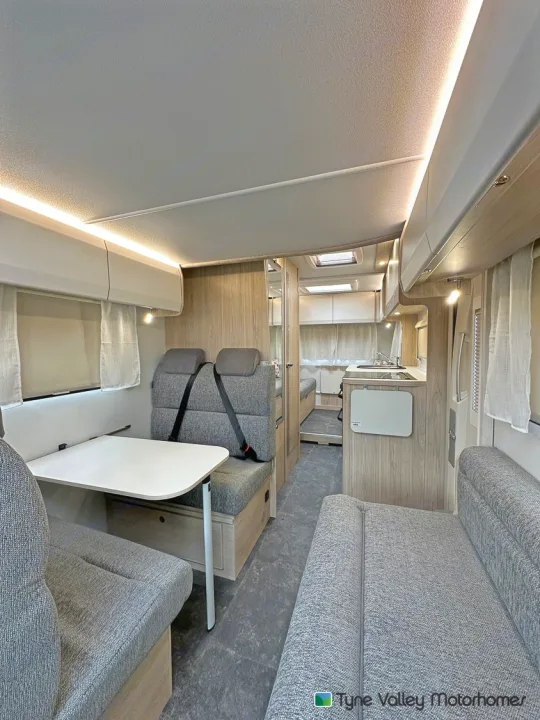Spacious RV rental interior: modern dinette, kitchen, and bed area. Light wood, grey upholstery, ambient lighting.. Elddis Whirlwind GT 196 2026