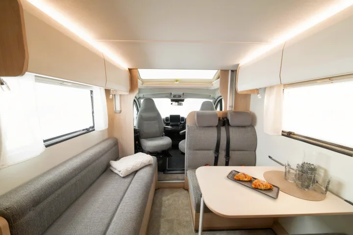 Bright rv rental interior: modern gray seating, dining table with croissants, and view into the driver's cabin.. Elddis Whirlwind GT 196 2026