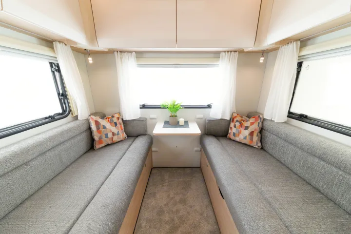 Bright RV rental lounge with grey fabric seating, a small table, windows, and overhead cupboards for compact living.. Elddis Whirlwind GT 196 2026