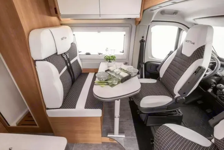 Modern RV rental interior: dinette with table set, front swivel seats, and passenger bench for comfortable campervan travel.. Giottiline 54T 2027