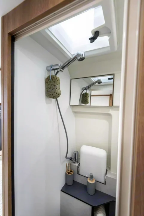 Step into this compact RV rental washroom, featuring a shower, toilet, mirror, and bright skylight.. Giottiline 54T 2027
