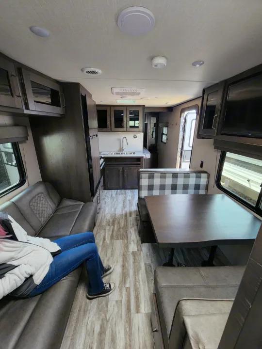 Explore this spacious and modern RV rental interior, showcasing a comfy living area, dining booth, kitchen, and bedroom access.. Grand Design Transcend Xplor 2022