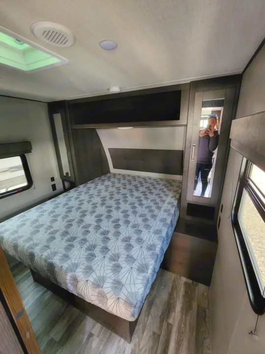 Explore this RV rental bedroom: a comfortable bed, mirrored closet, window, and overhead storage create a cozy travel space.. Grand Design Transcend Xplor 2022