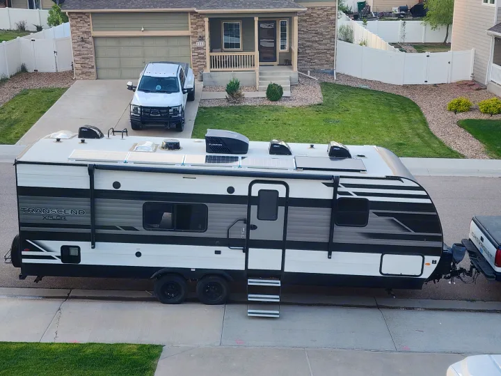 RV rental ready for adventure: A Transcend Xplor travel trailer with solar panels hitched to a pickup truck on a residential street.. Grand Design Transcend Xplor 2022