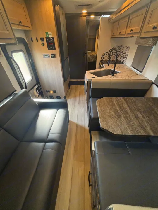 This RV rental interior features a sofa, dinette, and kitchen with a sink, all within a modern, clean design.. Forest River Sunseeker Classic 2025