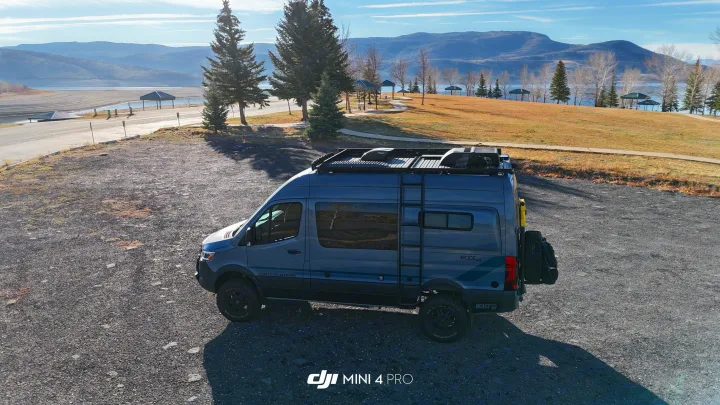 Storyteller Overland camper van (rv rental) on a gravel lot overlooking a scenic lake & mountains with shelters.. Storyteller Overland Storyteller Overland Class B 2023
