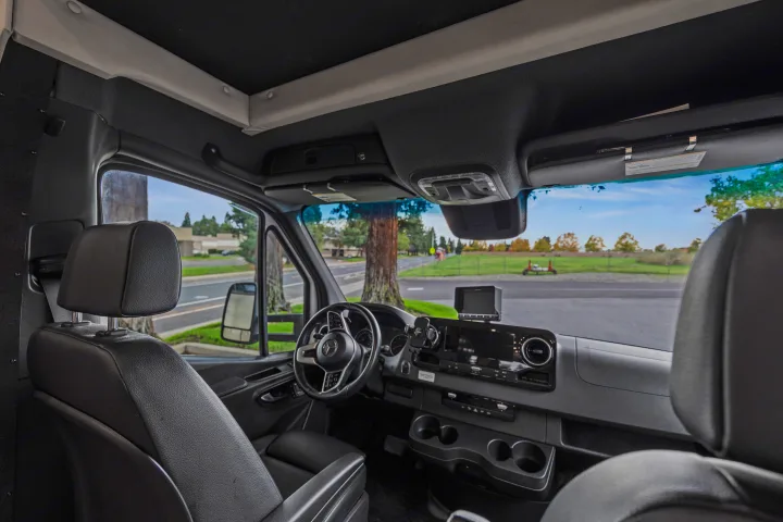 Spacious Mercedes-Benz RV rental interior, showing the modern dashboard, steering wheel, and front seats from the driver's perspective.. Dynamax Corp Isata 2021