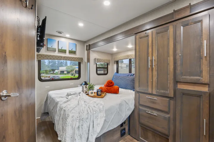 Inviting RV rental bedroom with a queen bed, plush bedding, windows, entertainment, and built-in wood cabinetry.. Dynamax Corp Isata 2021