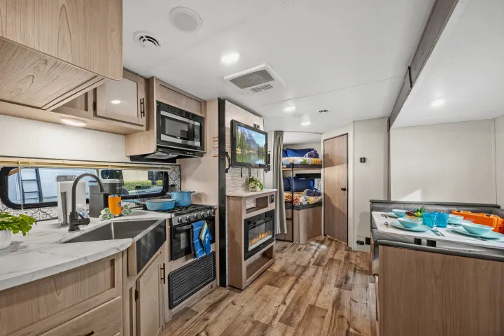 Modern RV rental interior featuring a full kitchen, dining booth, TV, fireplace, and cozy bunk beds.. Coleman Lantern 2022