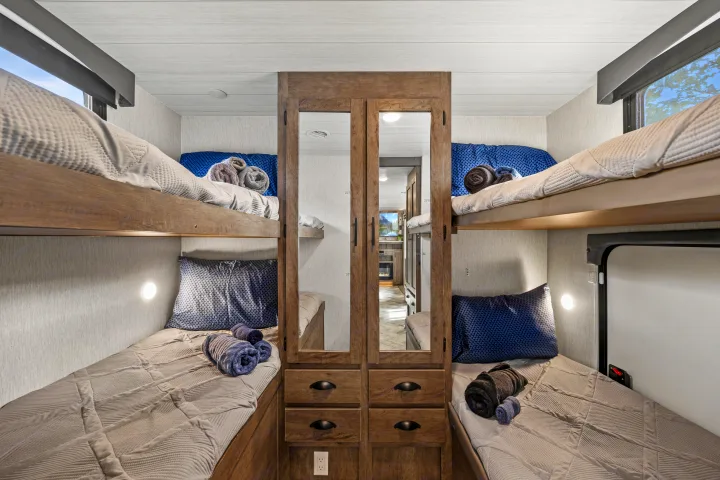 An RV rental bunk room with four beds, two on each side, a central wardrobe with mirrored doors, and individual lighting for cozy stays.. Forest River EVO CSJT2990 2022