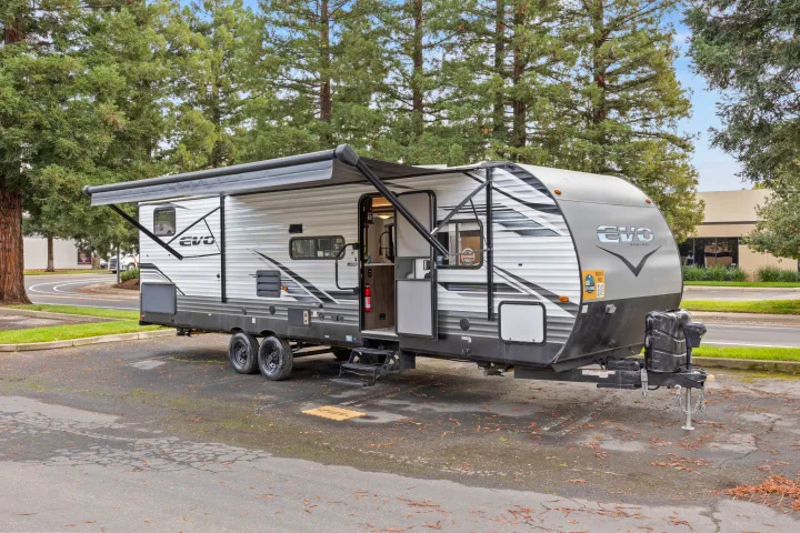 This gray and white travel trailer, featuring an extended awning and open door, is parked and ready for your RV rental adventure.. Forest River EVO CSJT2990 2022