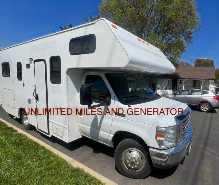 White RV rental with unlimited miles and generator, parked on a street under a clear sky. A car and house are in the background.. Thor Majestic 2019