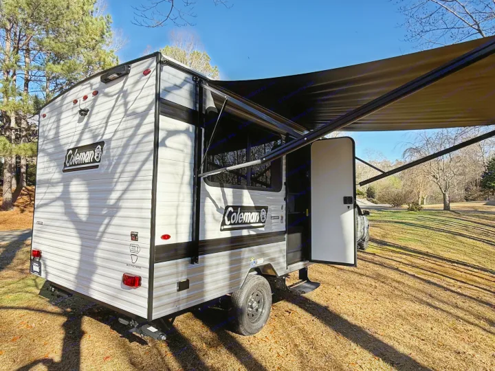 Enjoy the outdoors with this Coleman rv rental travel trailer, awning open, parked on grass under a blue sky.. Keystone Coleman 13R 2026