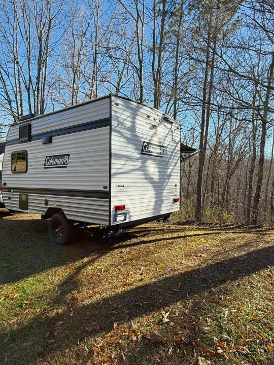 White Coleman rv rental parked among bare trees on a sunny fall day, shadows on the grass.. Keystone Coleman 13R 2026