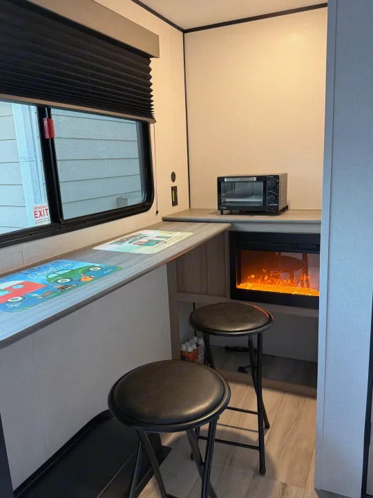 Cozy RV rental interior featuring a compact kitchenette with a toaster oven, dining counter with two stools, and an electric fireplace.. Keystone Coleman 13R 2026