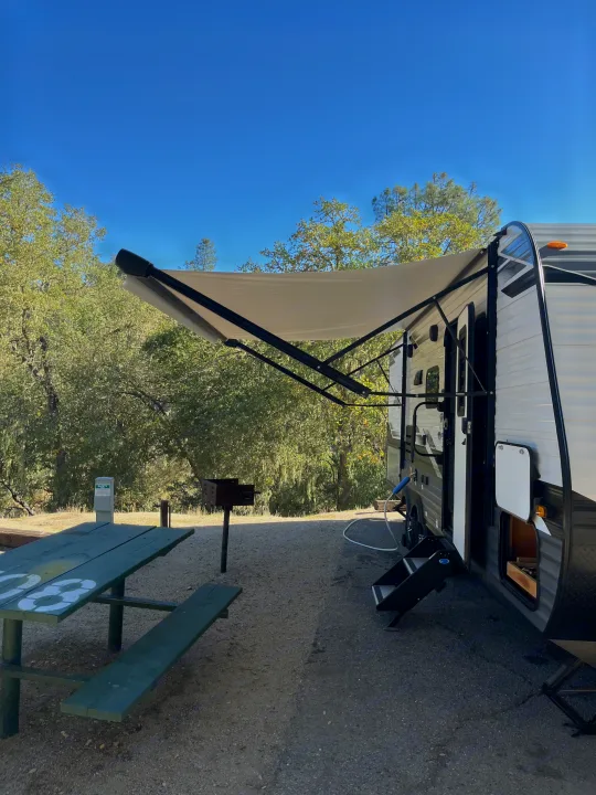 RV rental at a sunny campsite with an extended awning, picnic table, grill, and utilities.. Jayco Jay Flight SLX Rocky Mountain Edition 2022