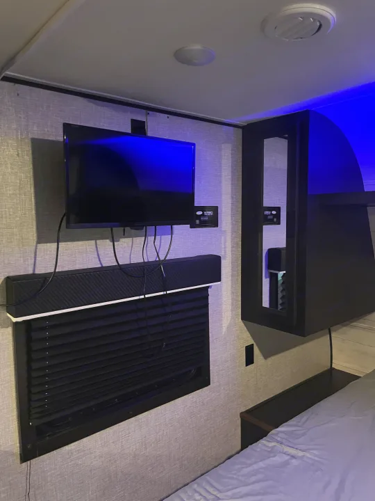 Modern RV rental bedroom with wall-mounted TV, soundbar, black blinds, and ambient blue lighting, creating a cozy and functional space.. Jayco Jay Flight SLX Rocky Mountain Edition 2022