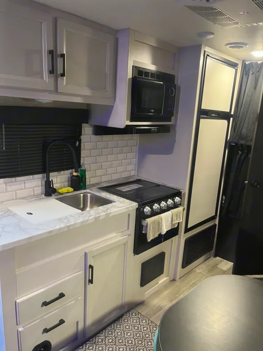 This rv rental kitchen features modern gray cabinets, white subway tile, a sink, microwave, and stove for compact living.. Jayco Jay Flight SLX Rocky Mountain Edition 2022