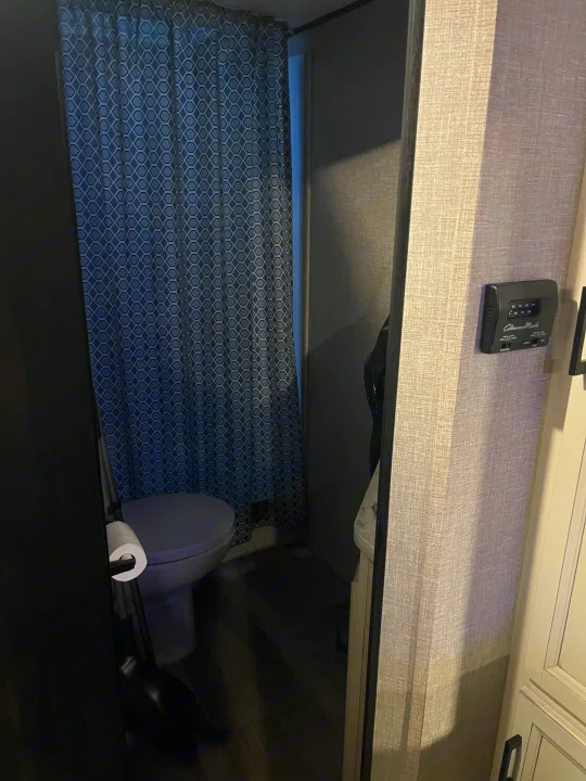 Compact RV rental bathroom with a gray toilet, geometric patterned shower curtain, and a Coleman-Mach thermostat.. Jayco Jay Flight SLX Rocky Mountain Edition 2022