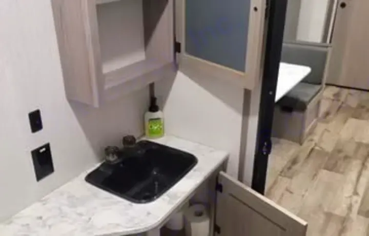 RV rental's compact vanity with sink and storage cabinets. A dinette is visible behind, offering a bright, functional interior for travel.. Dutchmen Coleman Lantern 2022