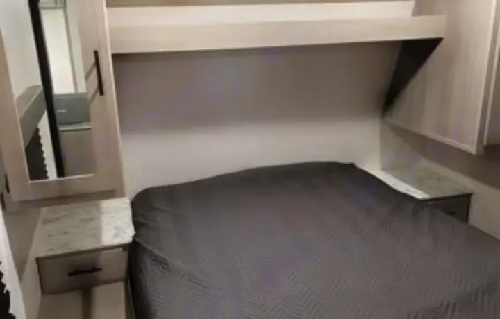 Cozy RV rental bedroom features a dark gray bed, nightstands, and overhead cabinets for comfortable travel.. Dutchmen Coleman Lantern 2022
