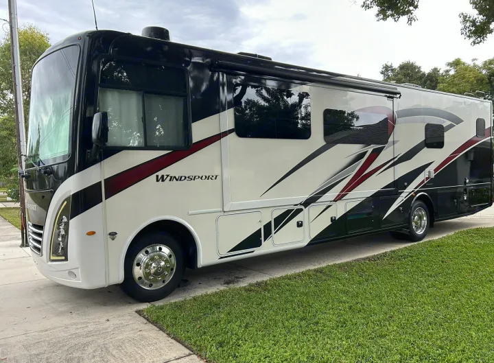 Modern Class A RV rental, sleek black, white & red design, parked on a driveway. Perfect for your next road trip!. Thor Windsport 2023