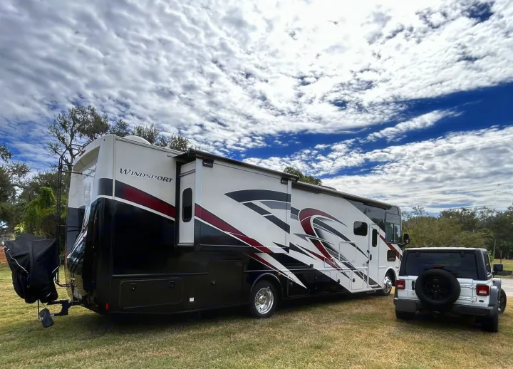 Spacious RV rental, a Thor Windsport motorhome, parked with a Jeep Wrangler on green grass under a partly cloudy sky. Ready for adventure!. Thor Windsport 2023