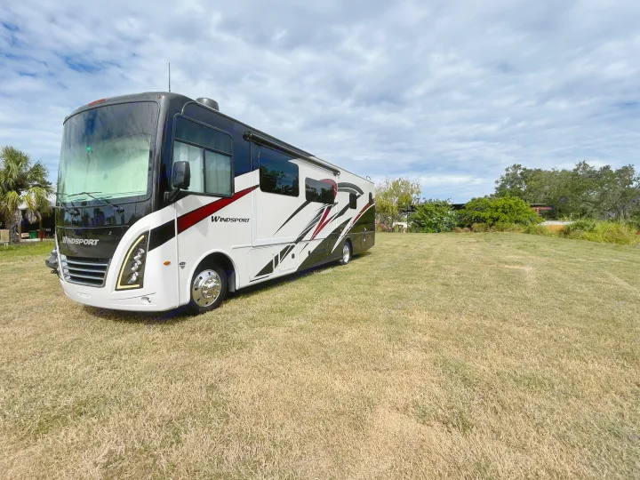 Modern black and white Windsport RV rental with red accents, parked on dry grass under a cloudy sky. Ready for travel.. Thor Windsport 2023