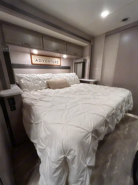 Cozy RV rental bedroom with modern design, white pintuck bedding, and an 'ADVENTURE' sign above the bed. Ready for travel!. Thor Windsport 2023