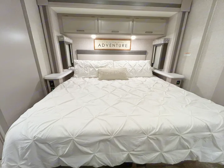 Comfortable RV rental bedroom with a white bed, pin-tucked comforter, and an 'ADVENTURE' sign above the headboard.. Thor Windsport 2023