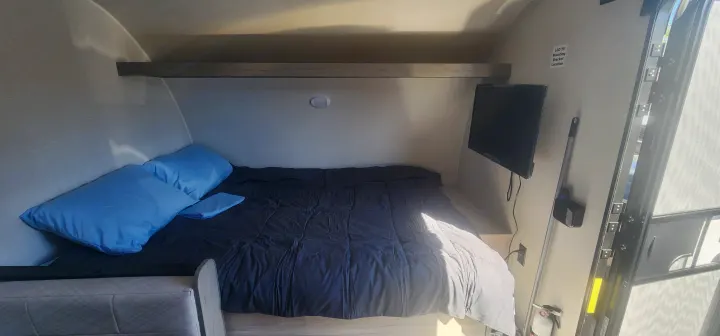 Cozy RV rental interior with a bed, blue pillows, TV, and shelf, offering a comfortable sleeping area for your travels.. Heartland Pioneer 2025