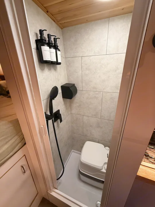 This RV rental features a modern, compact bathroom with tiled shower, black fixtures, and a portable toilet for your travels.. Dodge Pro Master High Roof 3500 Extended 2021