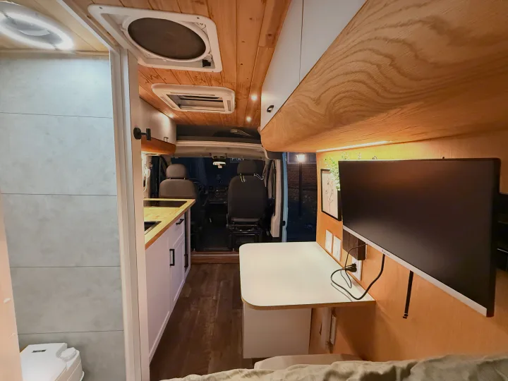 Stylish RV rental interior: a modern campervan with a kitchenette, desk, monitor, and compact bathroom on the left.. Dodge Pro Master High Roof 3500 Extended 2021