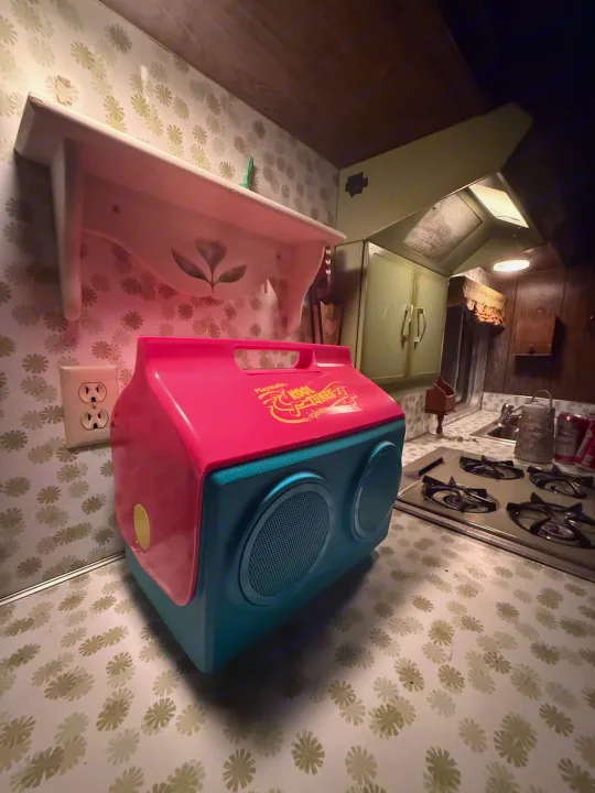 This vibrant pink and teal Igloo Kool Tunes cooler brightens a retro kitchen in an rv rental, featuring patterned walls and counters.. International 510A 1973