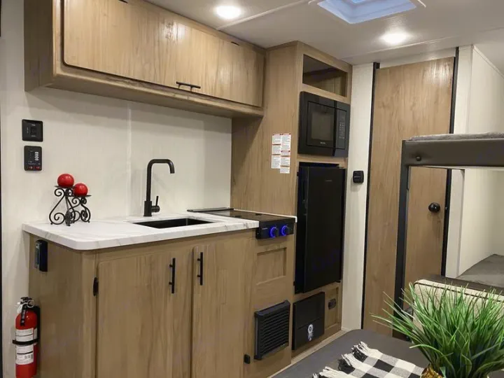 An inviting RV rental interior: modern kitchenette with sink, microwave, fridge, and adjacent cozy sleeping/dining space.. Forest River Cherokee Wolf Pup 2025
