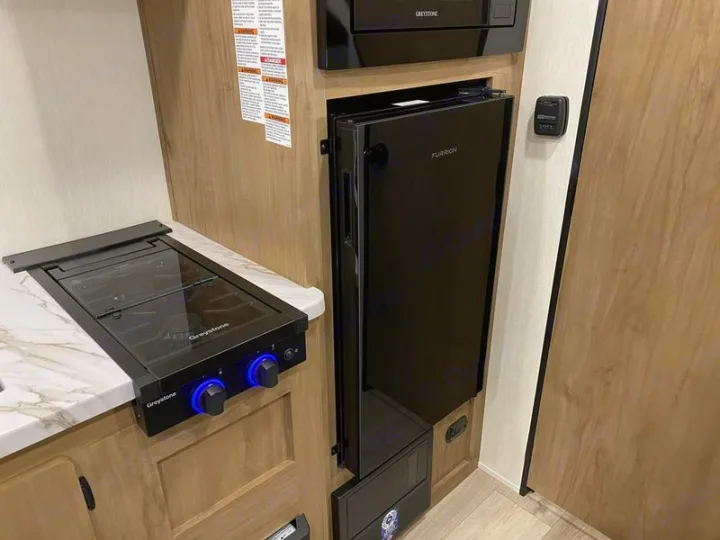 Compact RV rental kitchen featuring a Greystone two-burner cooktop, microwave, and a slim Furrion refrigerator. Ready for your trip!. Forest River Cherokee Wolf Pup 2025
