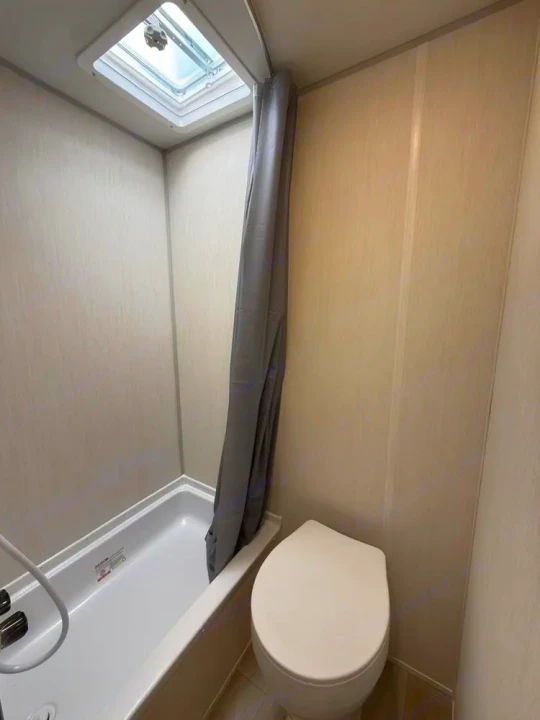 Compact RV rental bathroom features a white tub/shower with a gray curtain, toilet, and overhead skylight.. Forest River Cherokee Wolf Pup 2025