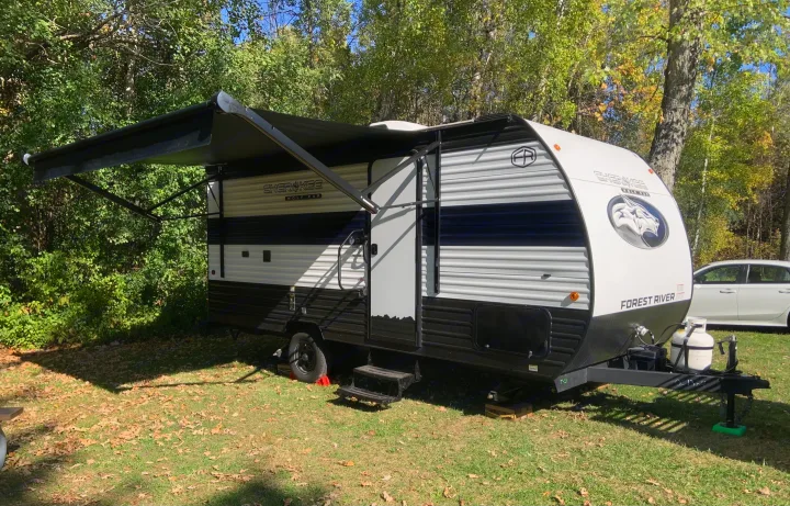 This Forest River Cherokee Wolf Pup RV rental is set up for camping under its awning, surrounded by fall trees.. Forest River Cherokee Wolf Pup 2025