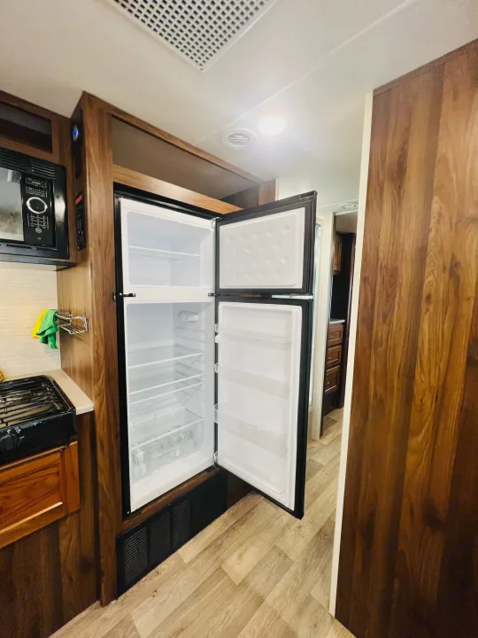 RV rental kitchen: open refrigerator, microwave, and stovetop in a warm, wood-finished interior. Ready for your adventure.. Winnebago Outlook 2020