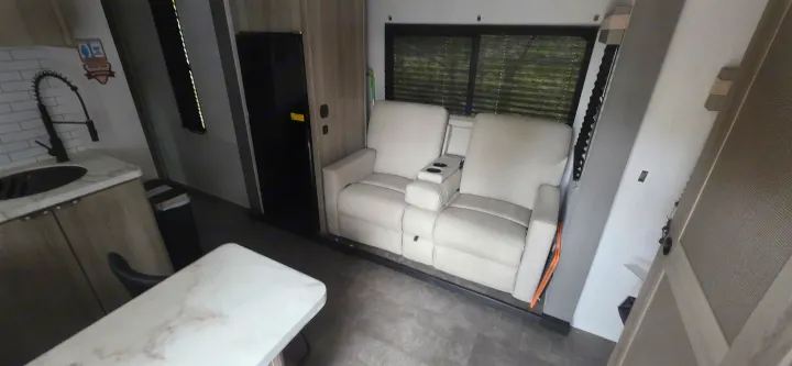 This rv rental features a compact kitchen with a modern sink, light wood cabinets, and comfortable theater recliners.. Forest River Wildwood FSX Platinum 2024