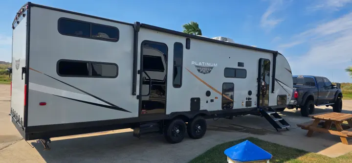 This light gray Platinum Wildwood FSX travel trailer makes an excellent rv rental for your next adventure. Parked with a truck under a bright sky.. Forest River Wildwood FSX Platinum 2024