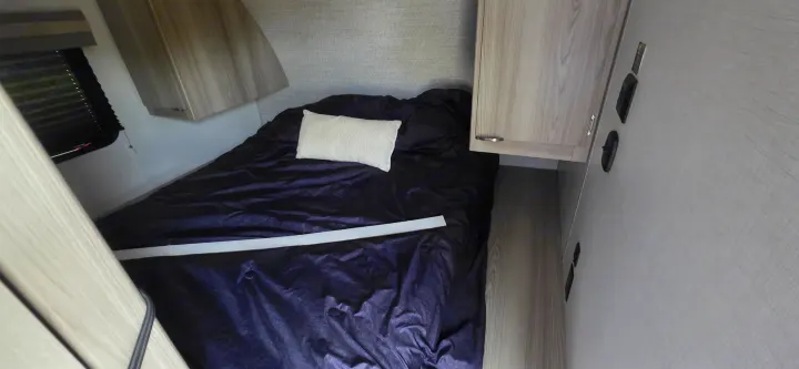 RV rental bedroom showing dark bed with pillow, light wood cabinets, and a window with dark blinds.. Forest River Wildwood FSX Platinum 2024