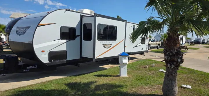 RV rental: A white Wildwood FSX Platinum travel trailer with its slide-out extended, parked at a sunny campground with a palm tree.. Forest River Wildwood FSX Platinum 2024