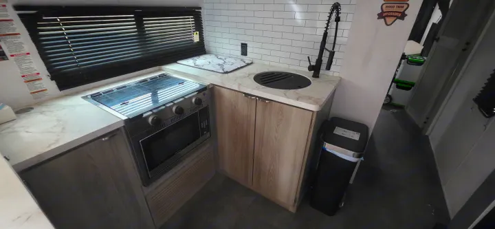 Modern rv rental kitchen with a stove, microwave, and sink, featuring sleek marble countertops and subway tile backsplash.. Forest River Wildwood FSX Platinum 2024