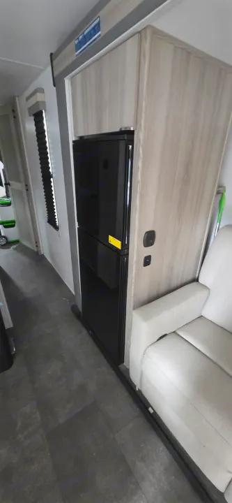 Cozy RV rental interior: black fridge built into light wood cabinetry, with a comfy light-colored sofa & dark floor.. Forest River Wildwood FSX Platinum 2024