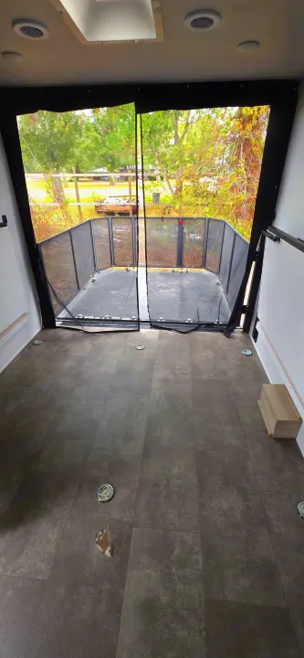 Inside an RV rental: toy hauler with screened rear patio. Gray tiled floor shows tie-downs & a damaged tile.. Forest River Wildwood FSX Platinum 2024