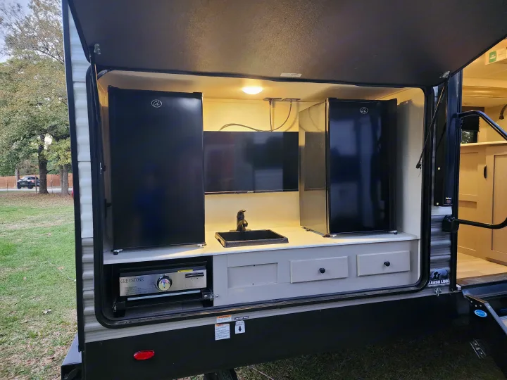 This RV rental outdoor kitchen boasts dual mini-fridges, a TV, sink, and Greystone griddle for convenient outdoor cooking.. Forest River Viking 6K 2025